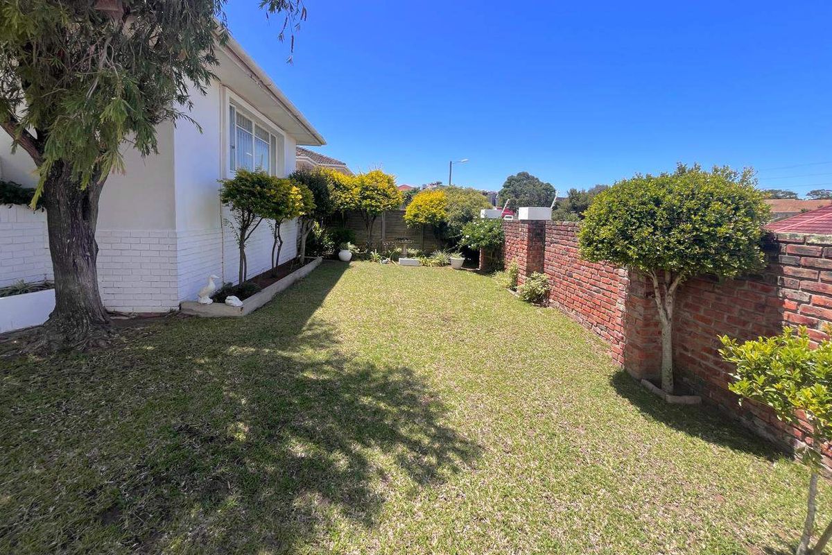 A well-maintained rear garden featuring a manicured lawn, established trees, and a classic red brick boundary wall.