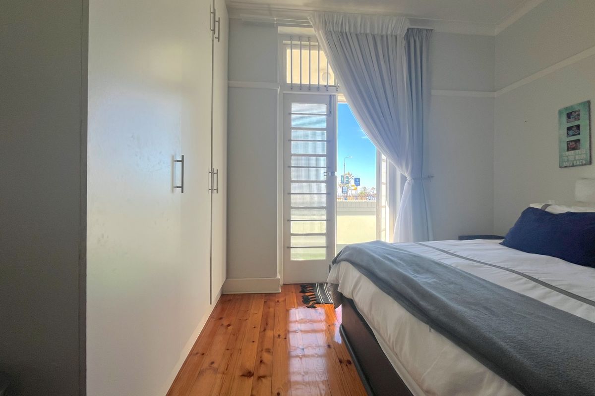 A bright bedroom featuring polished timber flooring, built-in floor-to-ceiling wardrobes, and a glass-panelled door providing access to an outdoor area.