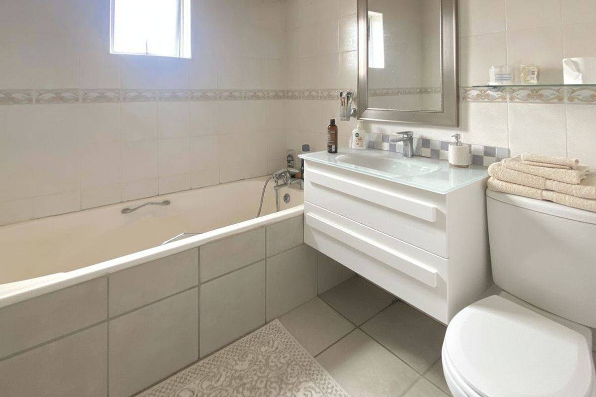 A functional bathroom featuring a built-in bathtub, a wall-mounted vanity with integrated sink, and a standard toilet with tiled walls and flooring.