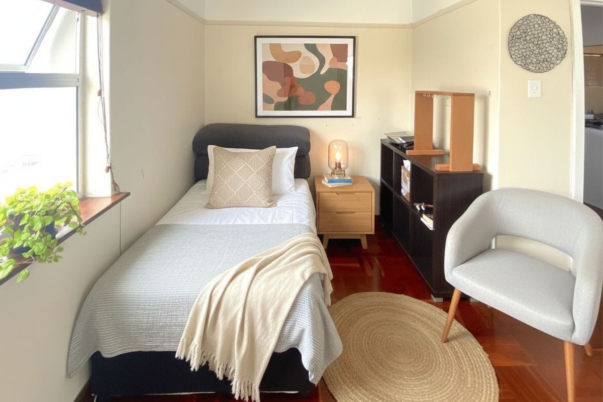 A compact bedroom featuring polished timber flooring, neutral wall tones, and a large window providing natural light.