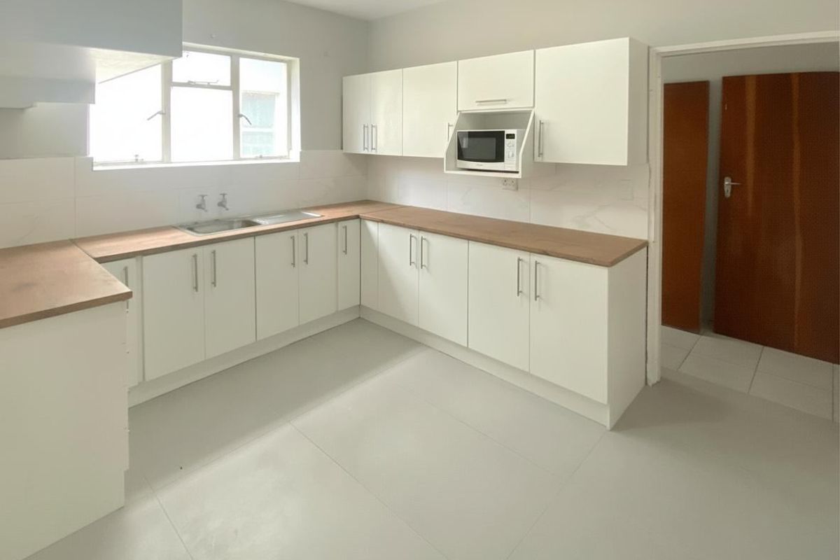 A clean, modern kitchen featuring white cabinetry, wood-look countertops, a stainless steel sink, and a built-in microwave.