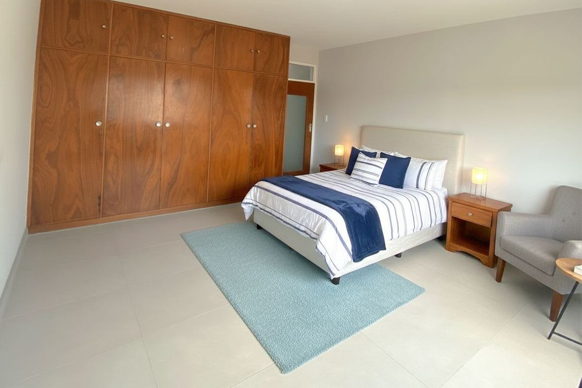 A spacious bedroom featuring large built-in wooden wardrobes, neutral tiled flooring, and a glass-paneled door.