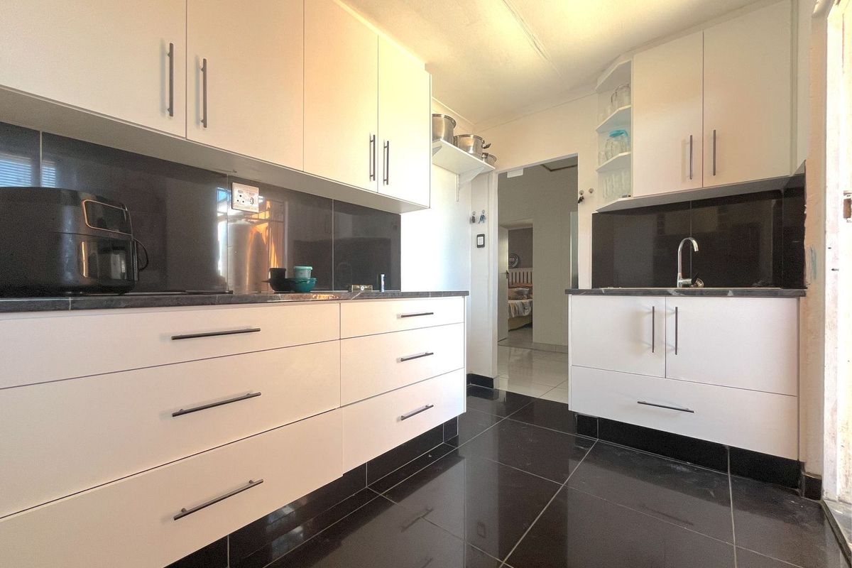 Modern kitchen featuring white cabinetry, dark stone countertops, black tiled splashbacks, and high-gloss black floor tiles.