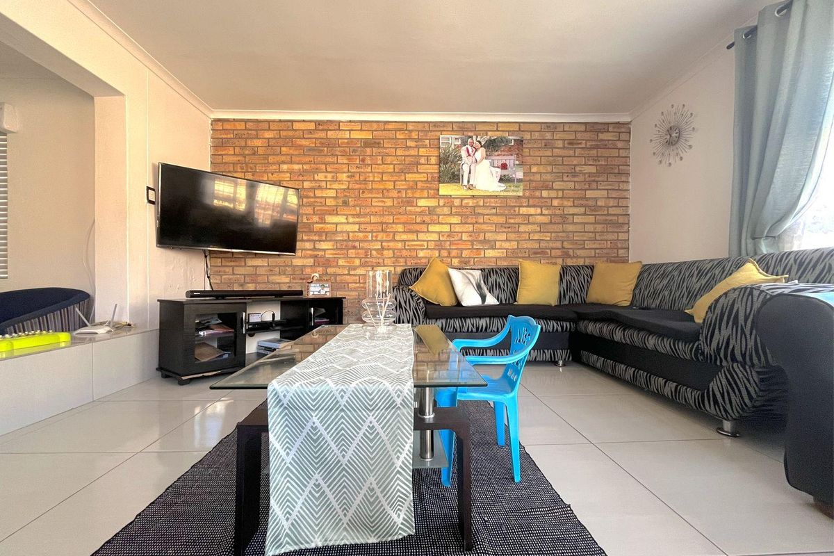 A living room featuring a prominent exposed brick feature wall and neutral floor tiling, providing a warm and textured focal point for the space.