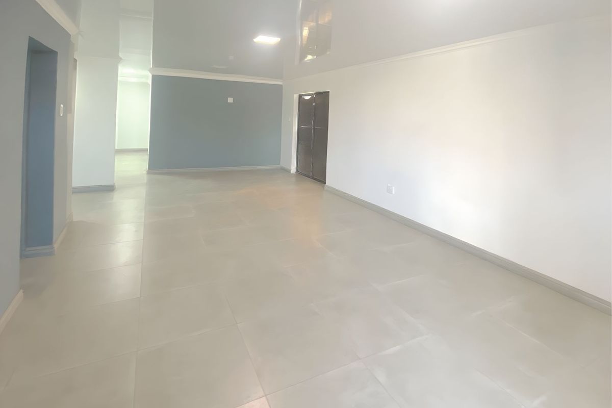 A spacious, empty living area featuring neutral tiled flooring, a glossy ceiling finish, and recessed lighting, offering a clean and versatile open-plan layout.