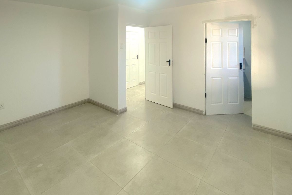 An empty, neutral-toned room featuring tiled flooring and multiple interior doors, providing a clean and versatile space ready for personalization.