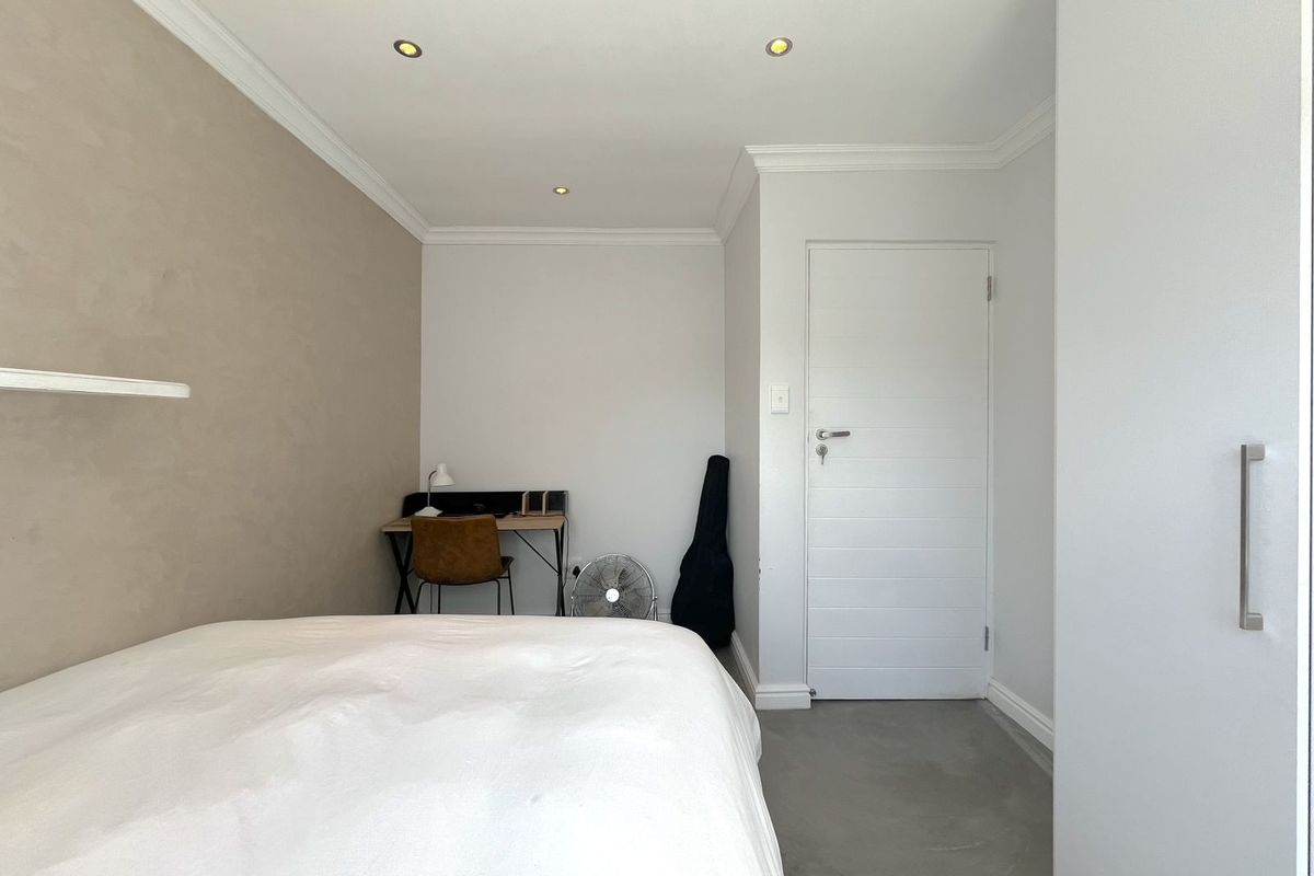 A well-maintained bedroom featuring neutral wall tones, recessed ceiling lighting, crown molding, and smooth concrete flooring.