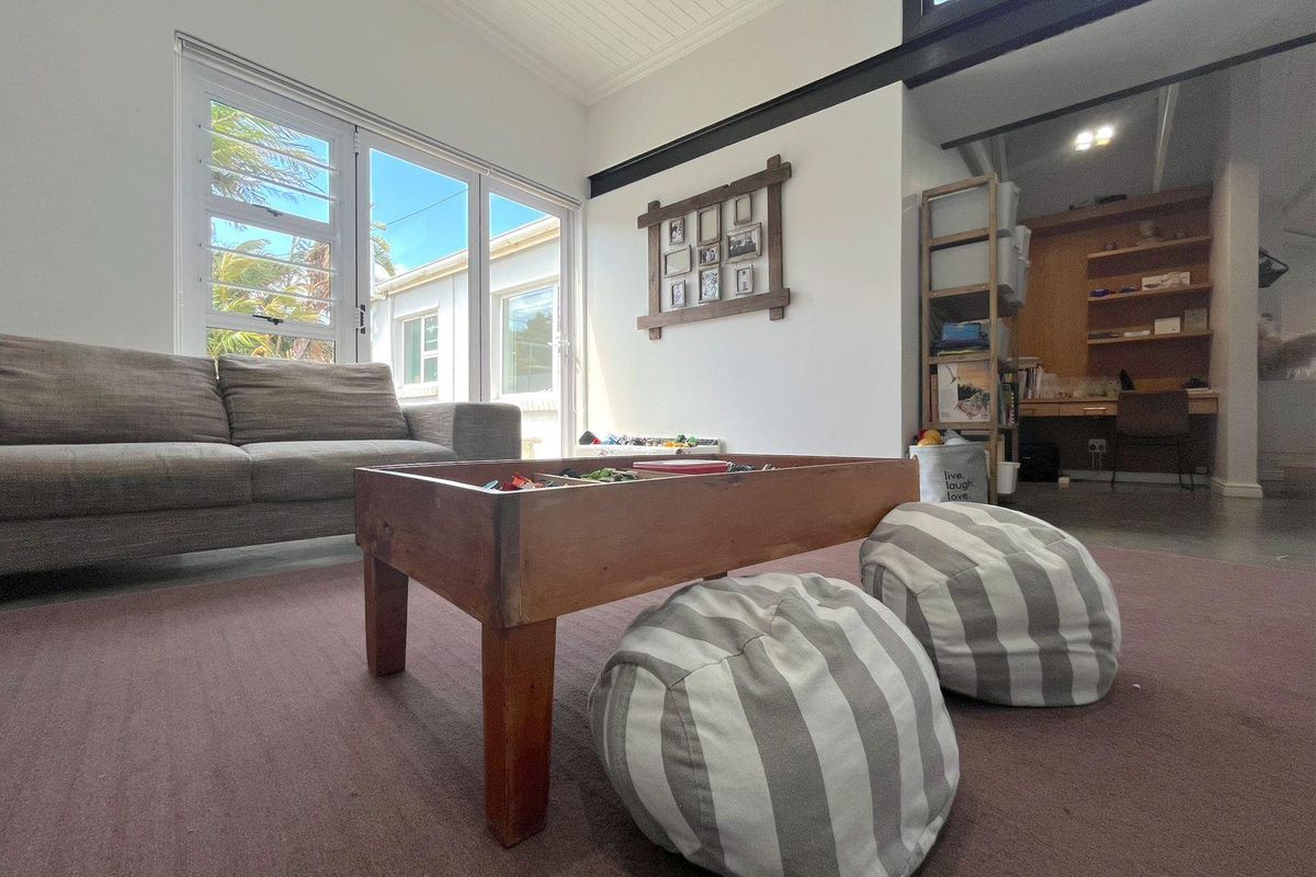 A bright living area featuring high ceilings, large windows, and a seamless transition to an adjacent study or workspace.