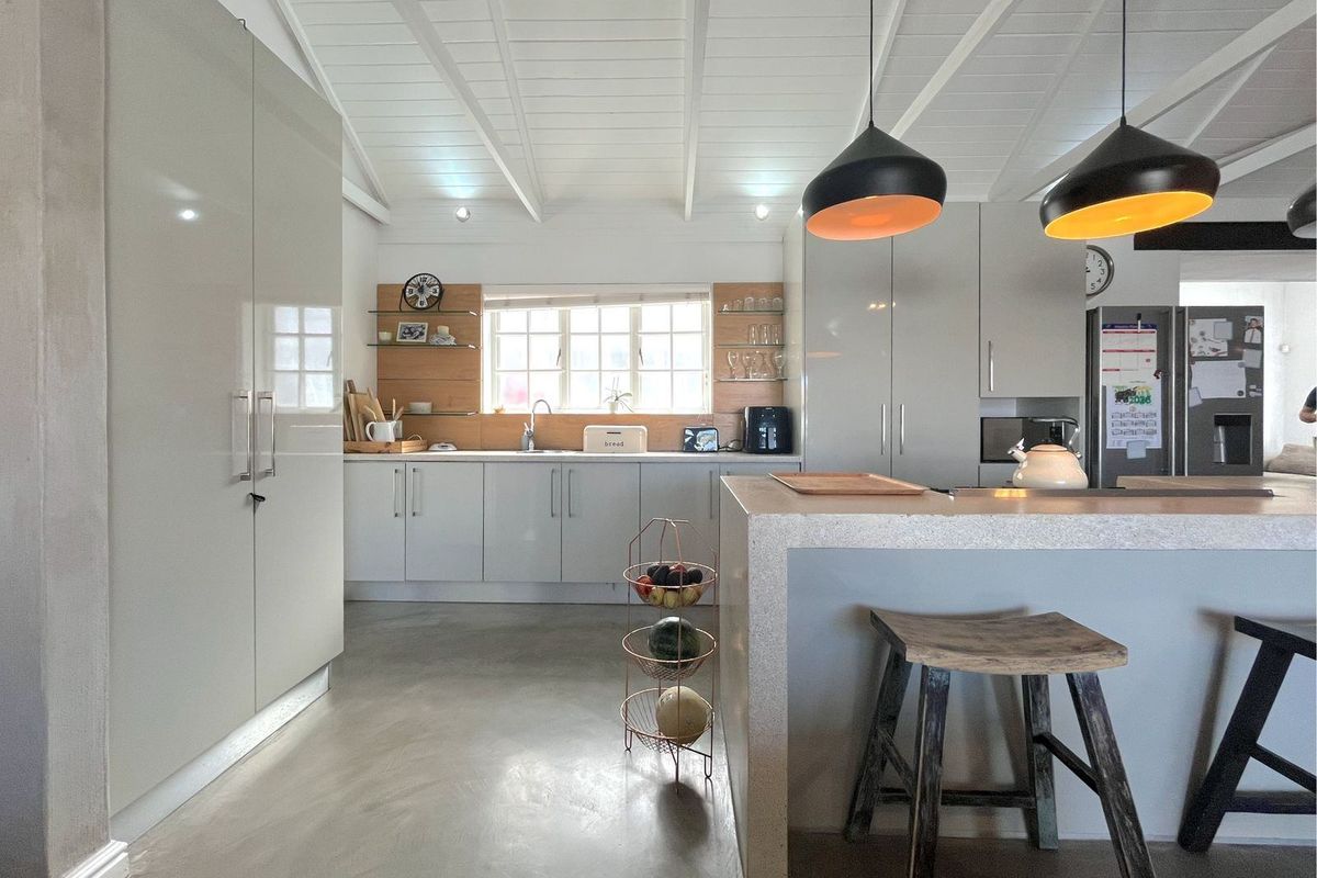 Modern kitchen featuring sleek cabinetry, a central island with breakfast bar seating, polished concrete flooring, and a vaulted timber-paneled ceiling.