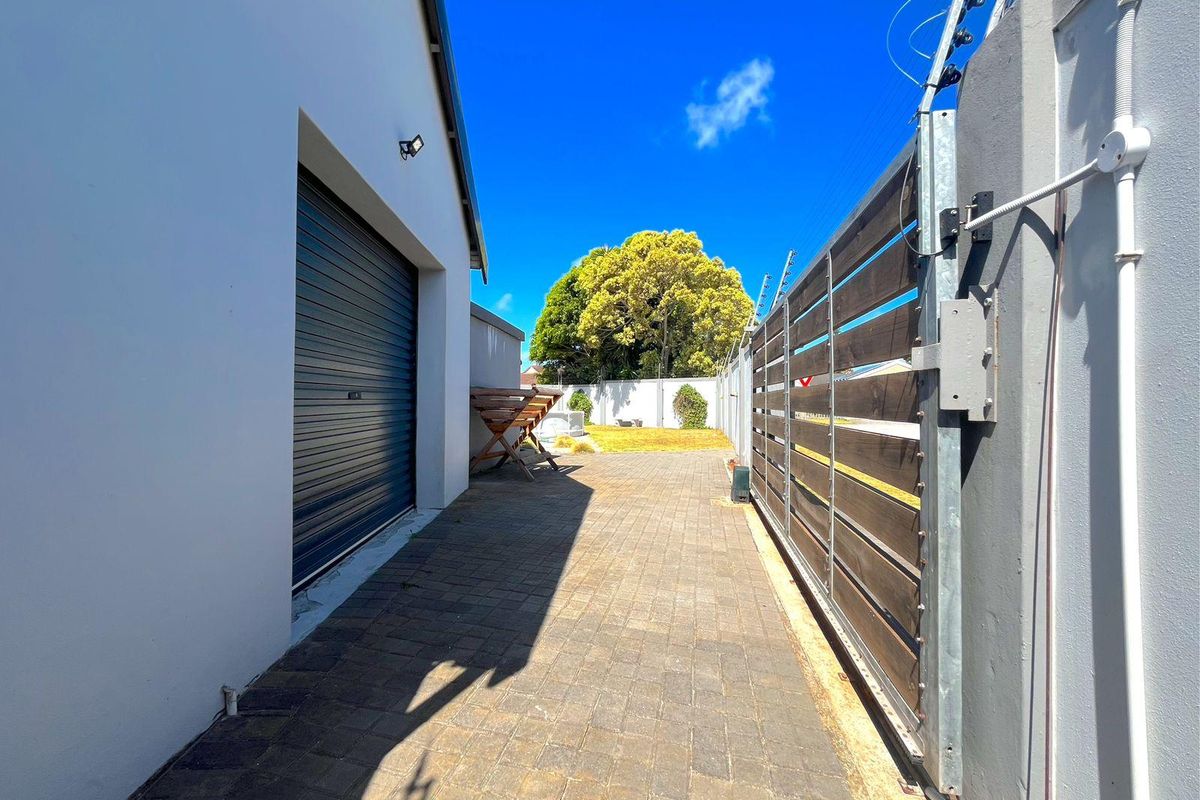 Side access path featuring paved driveway, roller garage door, and secure timber-slatted sliding gate with perimeter electric fencing.