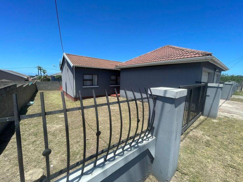 Rear view of the property featuring a tiled roof, enclosed garden area with perimeter walling, and metal security gate access.
