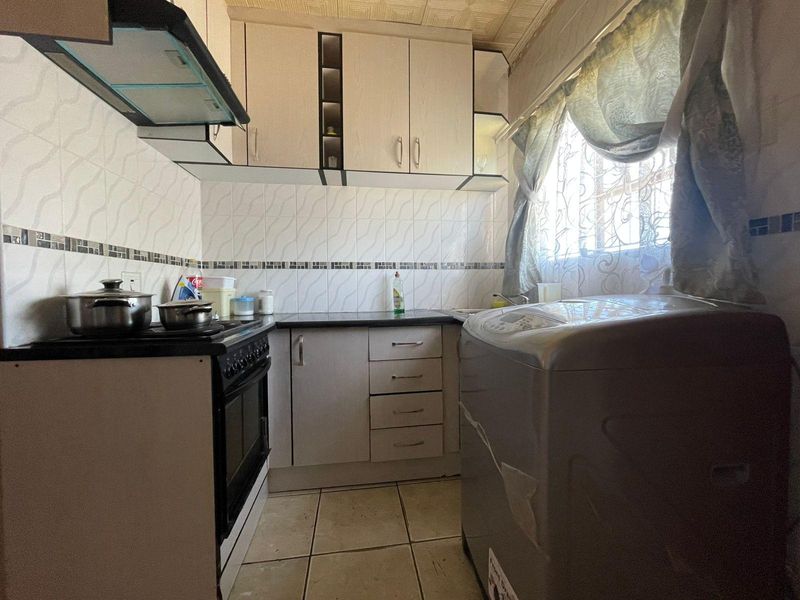Compact kitchen featuring built-in cabinetry, tiled splashbacks, and integrated stove with extractor fan, offering a functional layout with potential for modernization.