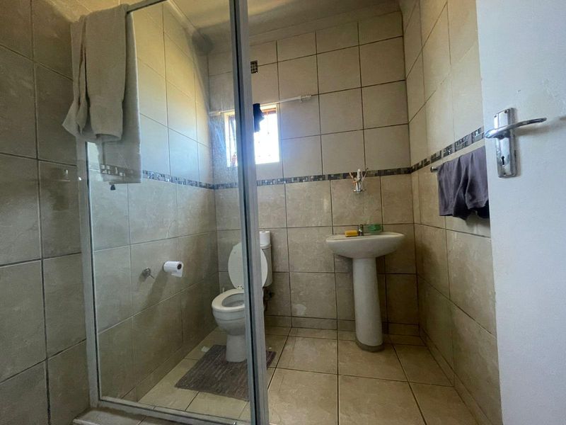 A compact bathroom featuring a pedestal basin, toilet, and a glass-enclosed shower with neutral wall and floor tiling.