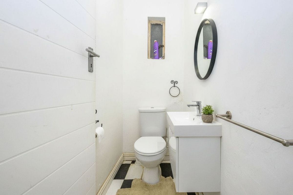 Compact guest bathroom featuring a modern vanity, wall-mounted mirror, and classic black and white checkered floor tiles.