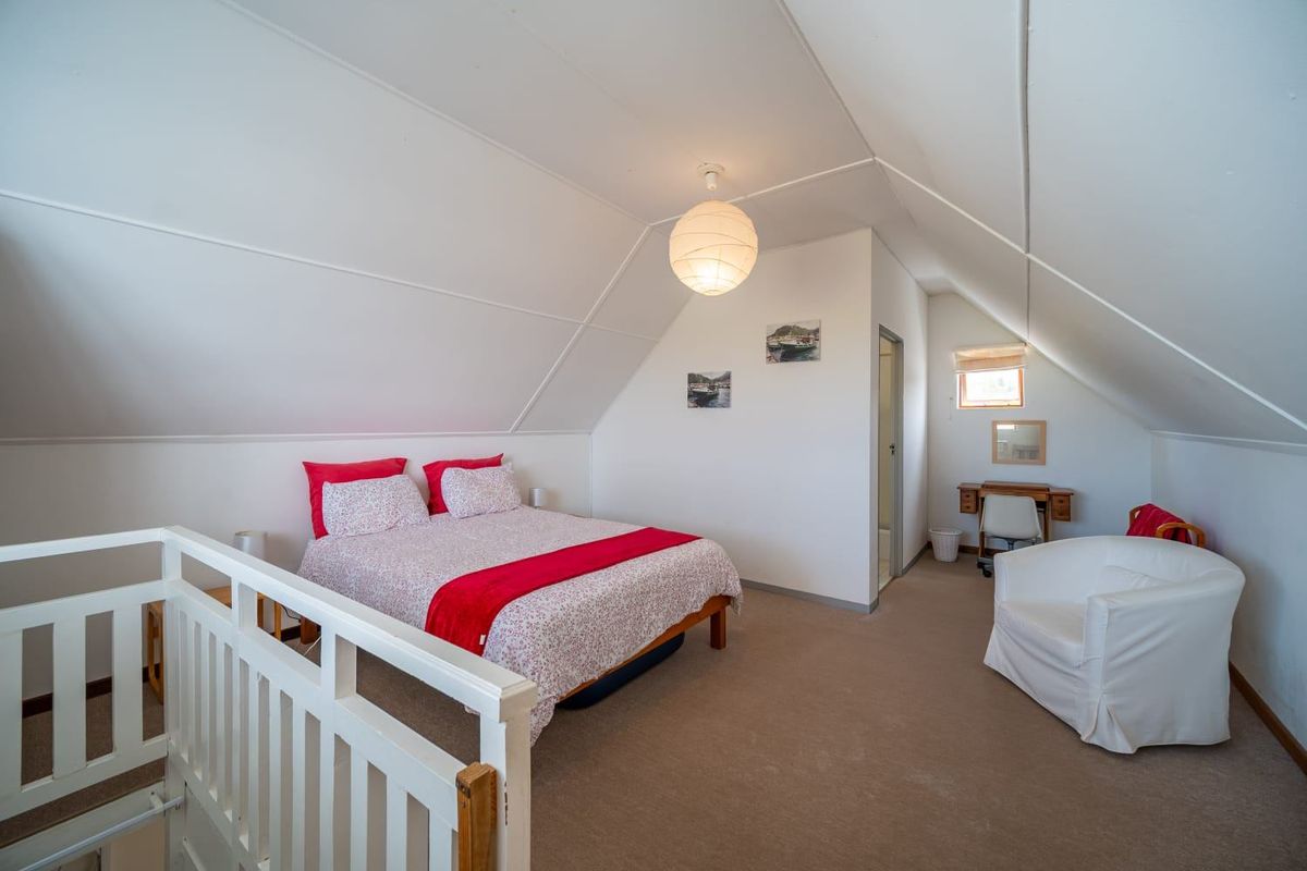 A spacious attic-style bedroom featuring sloped ceilings, neutral carpeting, and an integrated staircase railing, offering a cozy and functional living space.