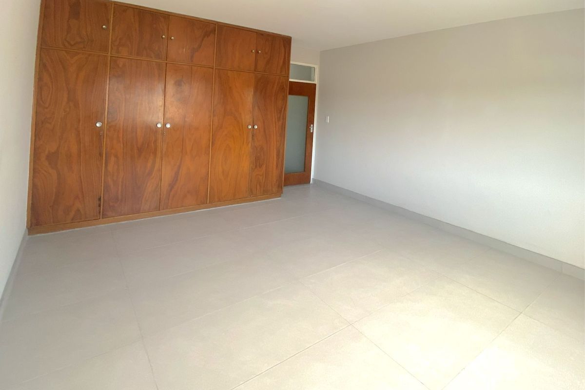 A spacious, empty bedroom featuring neutral tiled flooring and extensive built-in wooden cabinetry for storage.