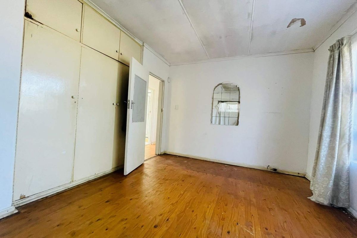 A bedroom featuring built-in cupboards, wooden flooring, and a recessed wall mirror, requiring cosmetic updates to restore its appeal.
