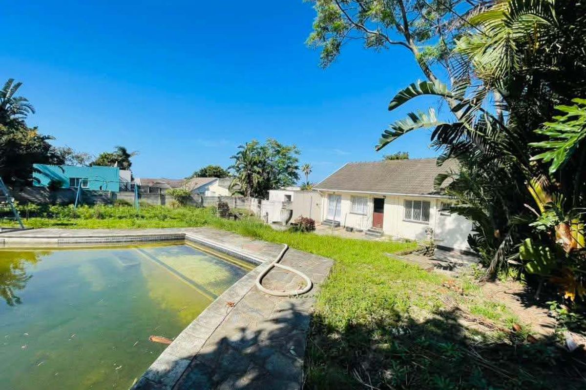 Rear view of the property featuring a swimming pool, paved surround, and a large garden area requiring maintenance.