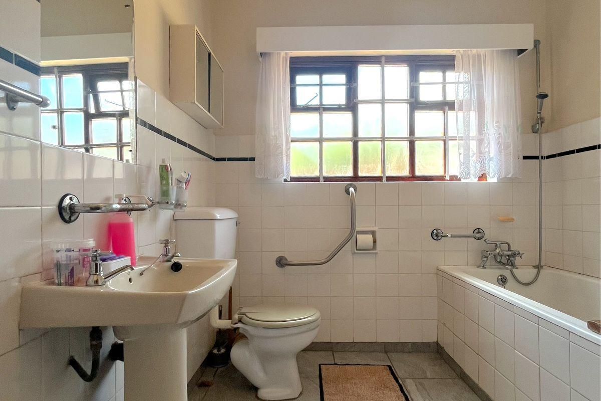 A functional bathroom featuring a pedestal sink, toilet with grab rail, and a bathtub with shower attachment, finished with classic wall tiling.