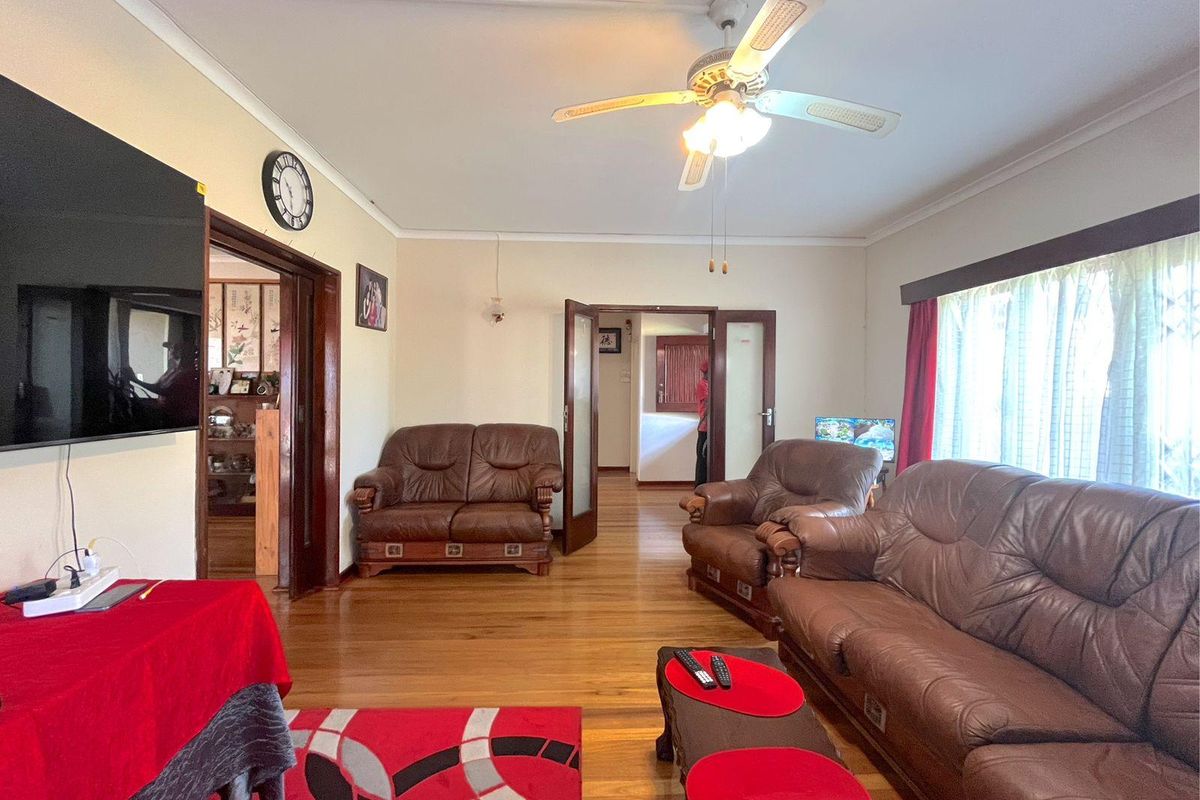 Spacious living room featuring polished timber flooring, a ceiling fan, and multiple access points to adjacent rooms.