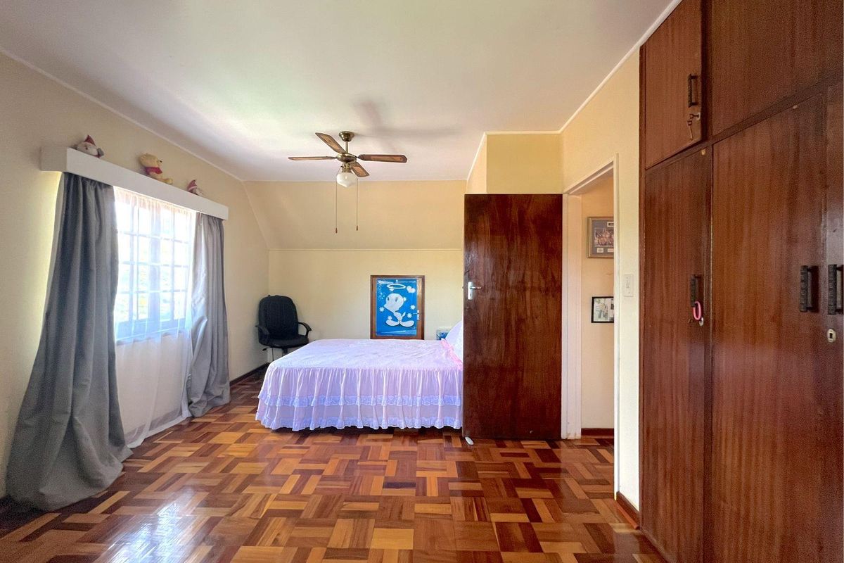 A bedroom featuring polished parquet flooring, built-in wooden cupboards, and a ceiling fan, offering a functional and traditional living space.