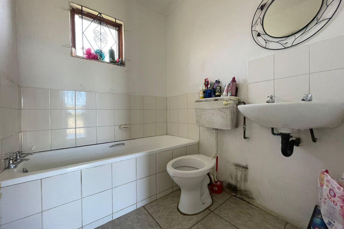 A dated bathroom featuring a built-in bathtub, standard toilet with high-level cistern, wall-mounted basin, and tiled splashbacks.