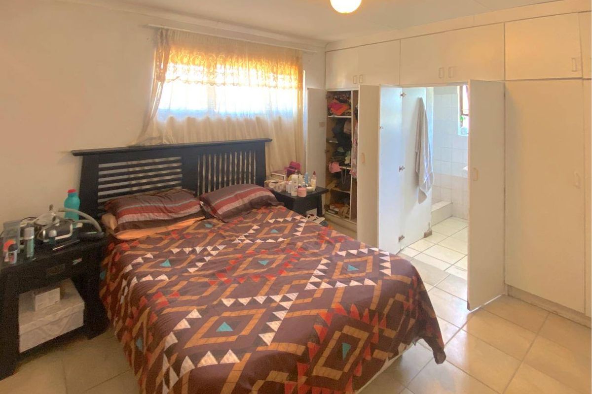 A bedroom featuring built-in cupboards and an en-suite bathroom, with tiled flooring and basic finishes throughout.