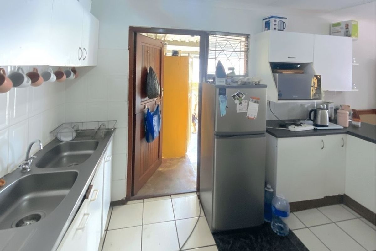 Functional kitchen featuring white cabinetry, double stainless steel sink, and tiled flooring with direct access to an outdoor area.