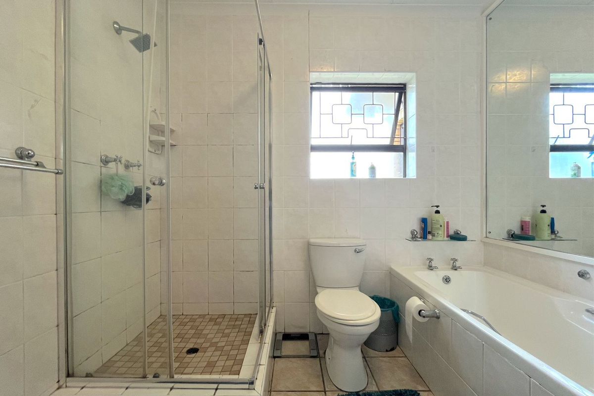A functional bathroom featuring a glass-enclosed shower, a built-in bathtub, a toilet, and a large wall-mounted mirror.