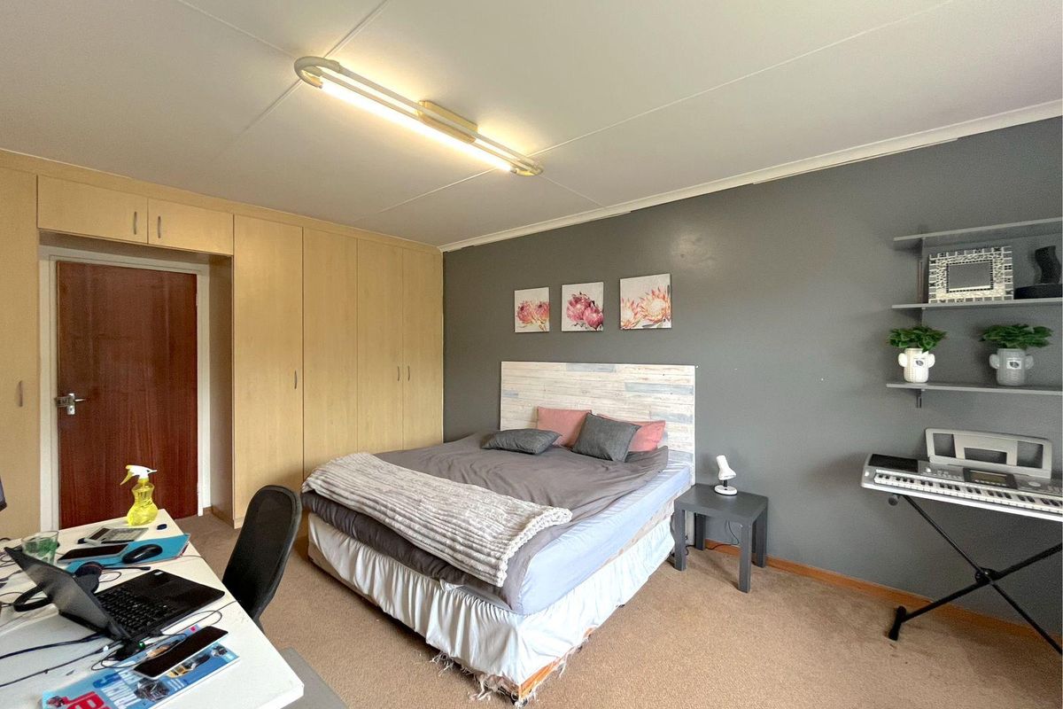 A bedroom featuring built-in wooden cabinetry, a grey accent wall, and carpeted flooring.