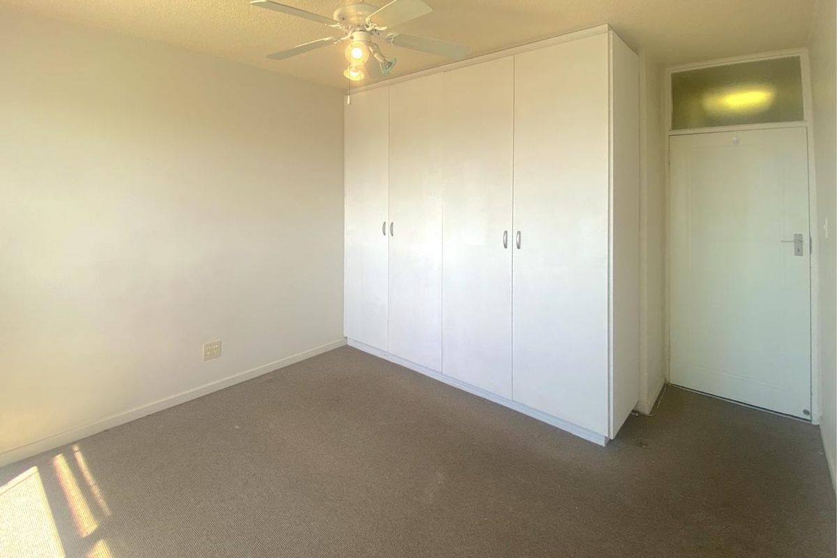 A bedroom featuring built-in wardrobes, a ceiling fan, and neutral carpeting, offering a clean and functional space.