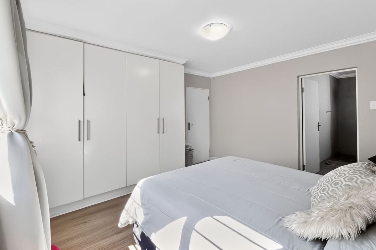 A well-maintained bedroom featuring built-in wardrobes, laminate flooring, and crown molding, offering a clean and neutral living space.