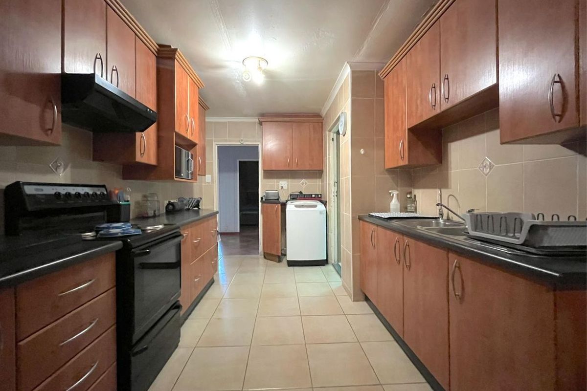 A functional galley-style kitchen featuring wood-tone cabinetry, dark countertops, tiled flooring, and a built-in extractor fan.