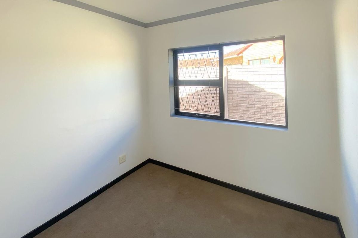 A vacant bedroom featuring neutral walls, carpeted flooring, and a window fitted with security bars.