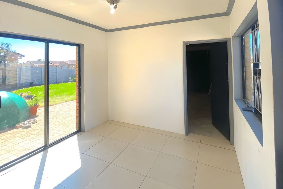 A bright, empty room featuring neutral floor tiles, a sliding glass door leading to the garden, and a doorway connecting to an adjacent space.