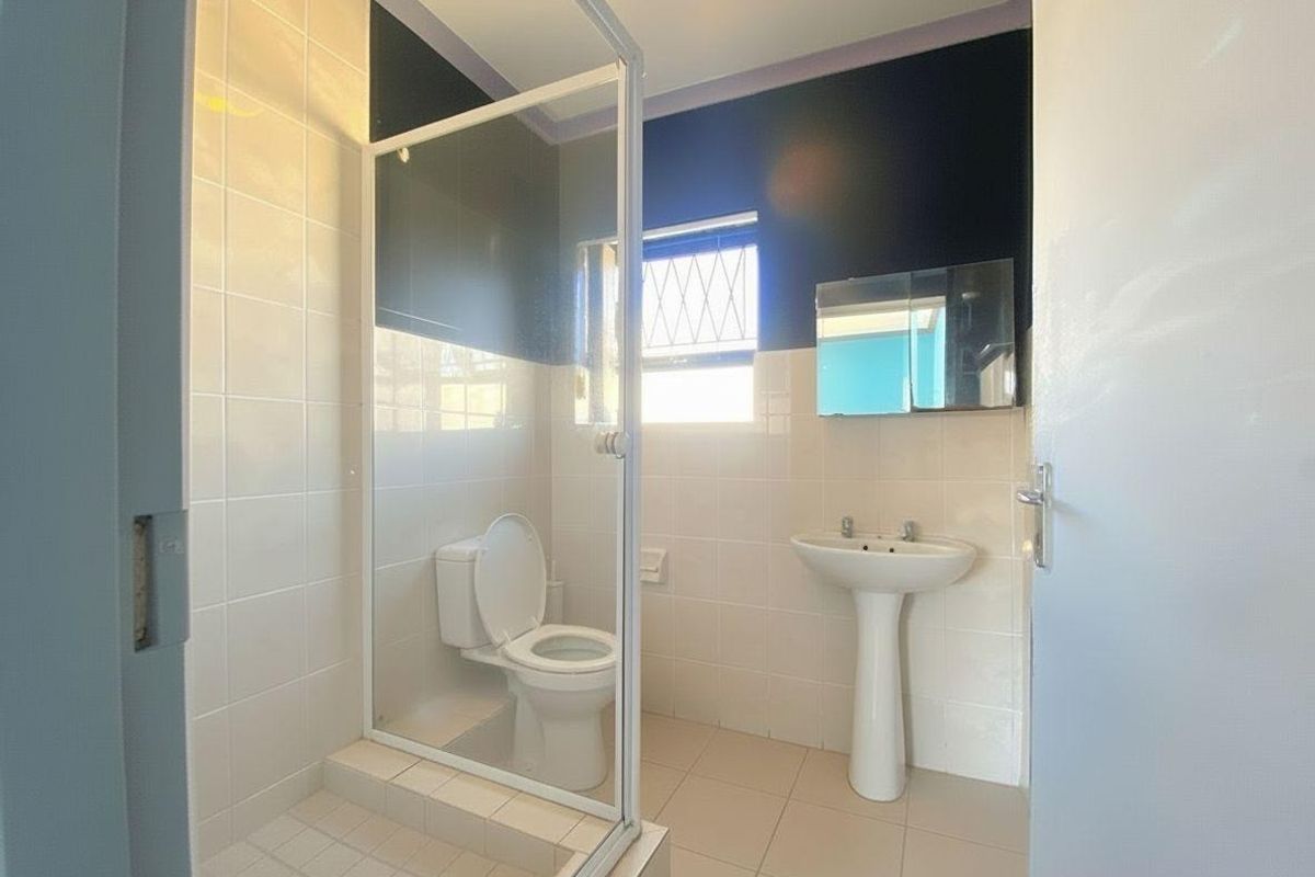 A functional bathroom featuring a glass-enclosed shower, pedestal basin, and toilet with tiled flooring and walls.
