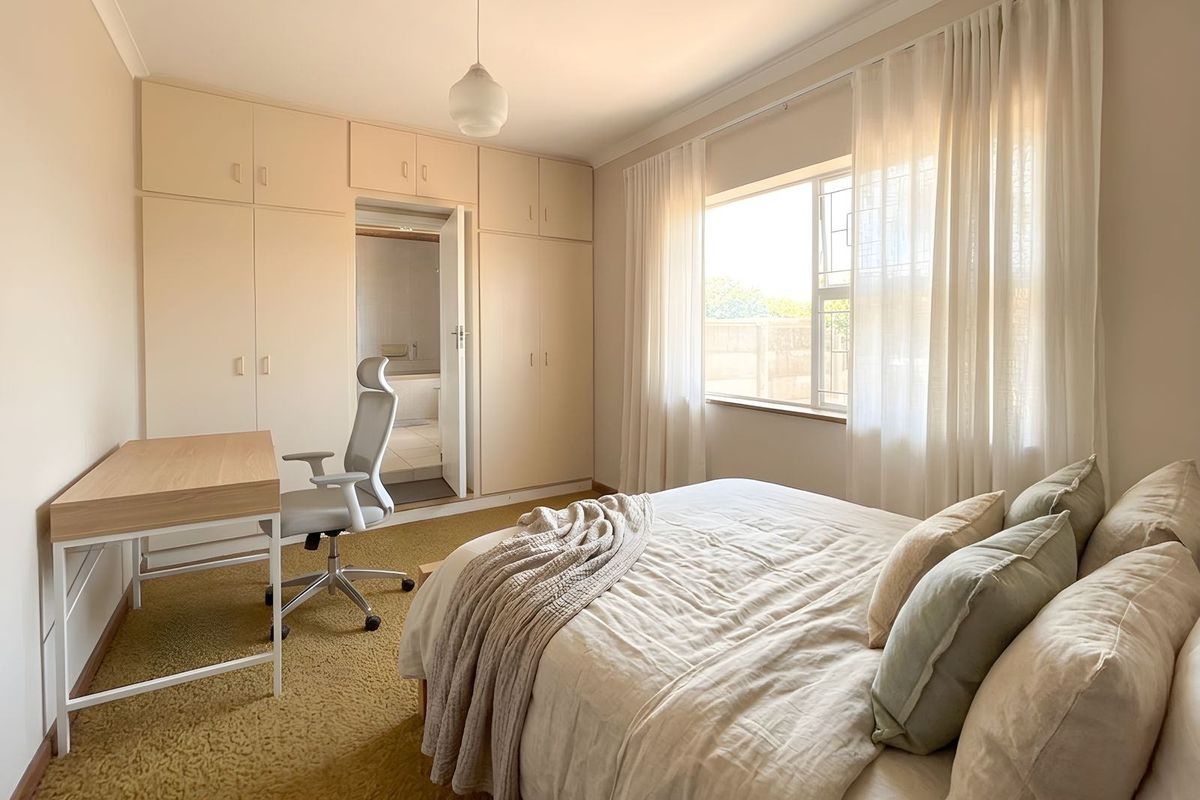 A well-lit bedroom featuring built-in cabinetry, carpeted flooring, and an en-suite bathroom access.