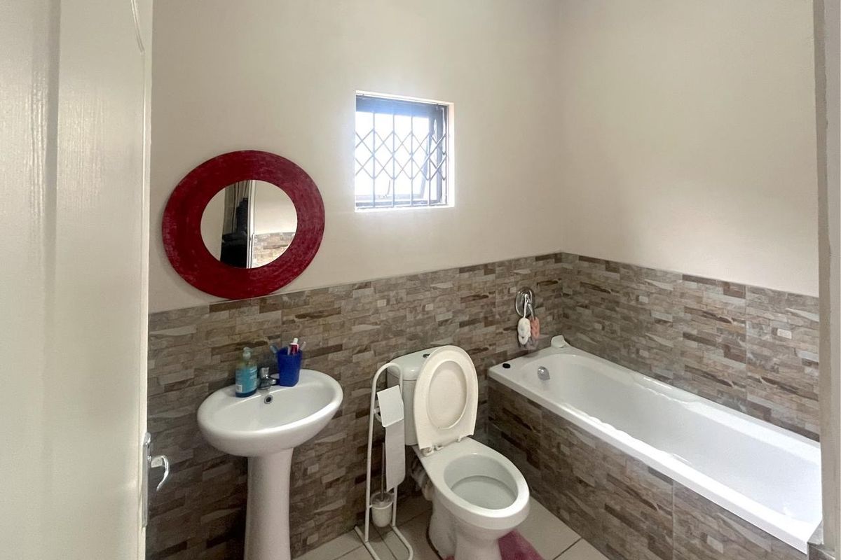 A functional bathroom featuring a pedestal basin, a standard toilet, and a built-in bathtub with decorative stone-look wall tiling.