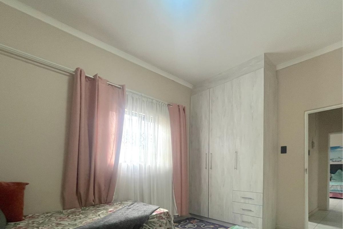 A bedroom featuring built-in cupboards with a light wood finish, tiled flooring, and a window with security bars.