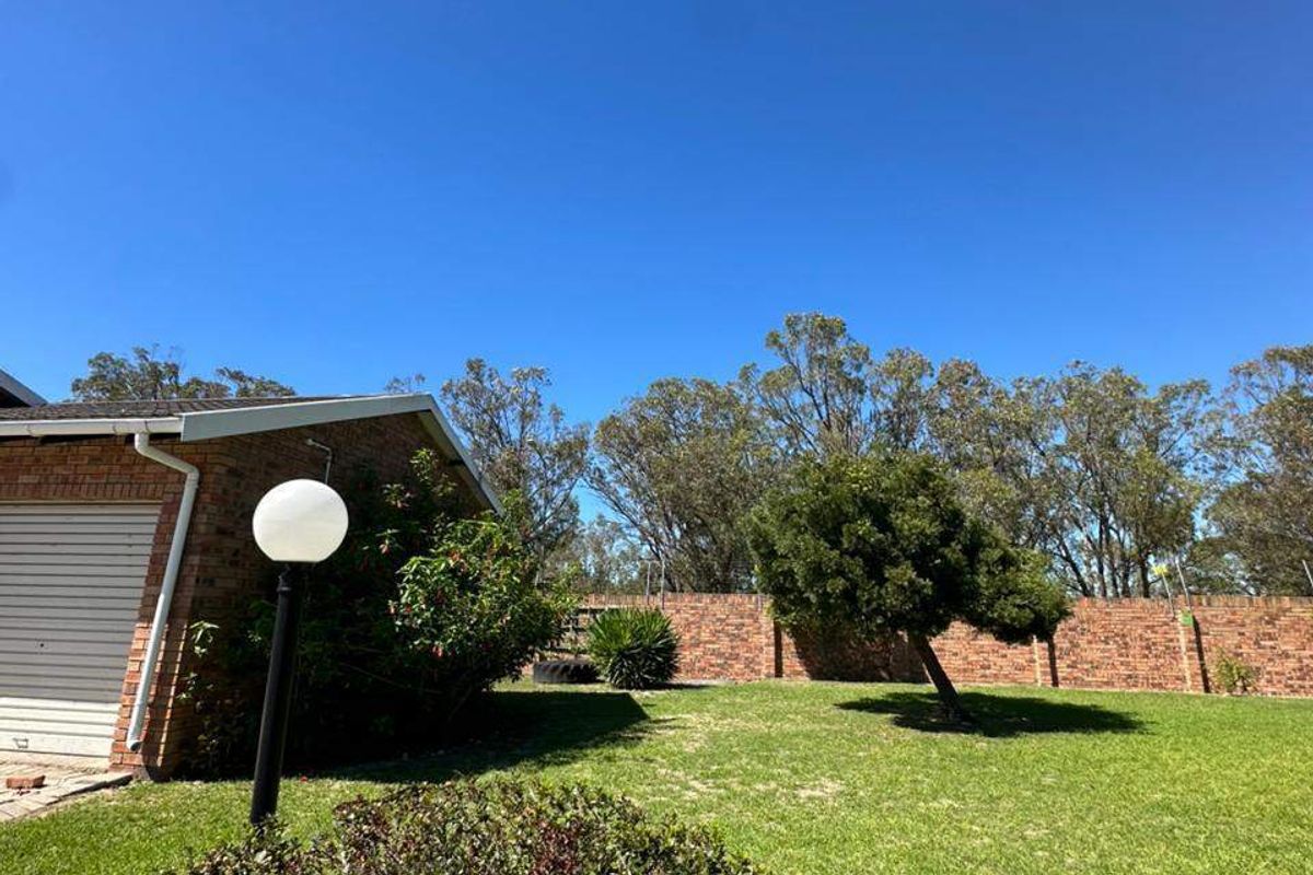 A view of the rear garden featuring a brick boundary wall, established trees, and a lawn area adjacent to the townhouse structure.
