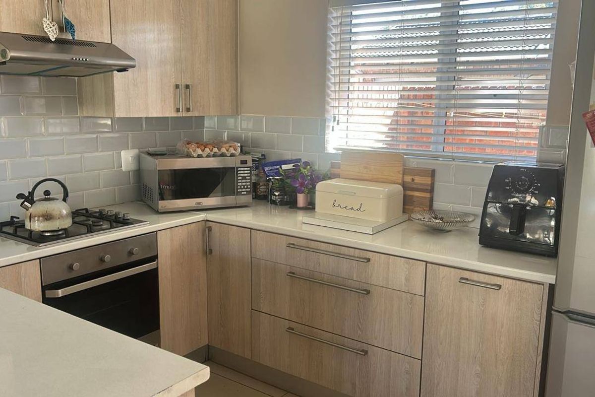 Modern kitchen featuring light wood-grain cabinetry, white stone countertops, subway tile backsplash, built-in oven, gas hob, and stainless steel extractor fan.