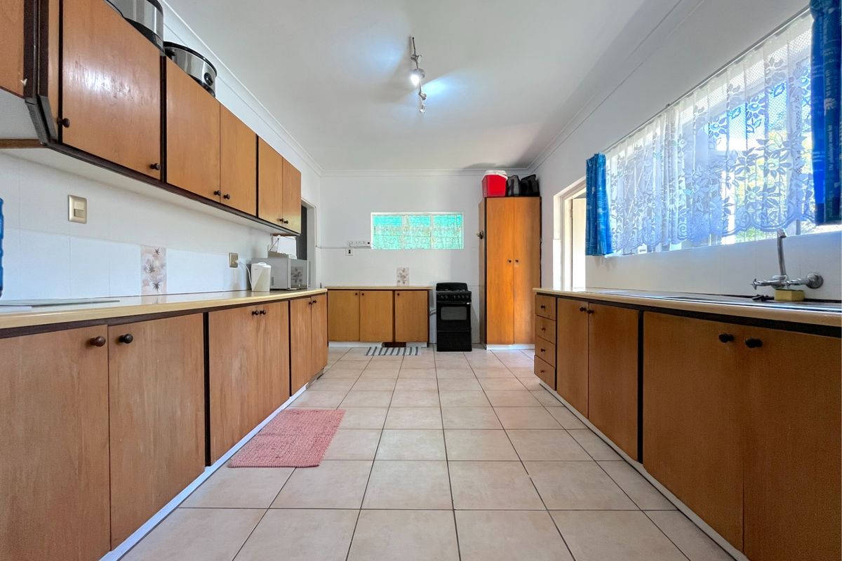 A spacious, functional kitchen featuring extensive wooden cabinetry, tiled flooring, and a freestanding stove, offering a classic layout ready for modern updates.