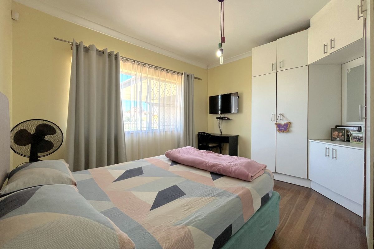 A well-lit bedroom featuring built-in white cabinetry, laminate flooring, and a window with security bars.