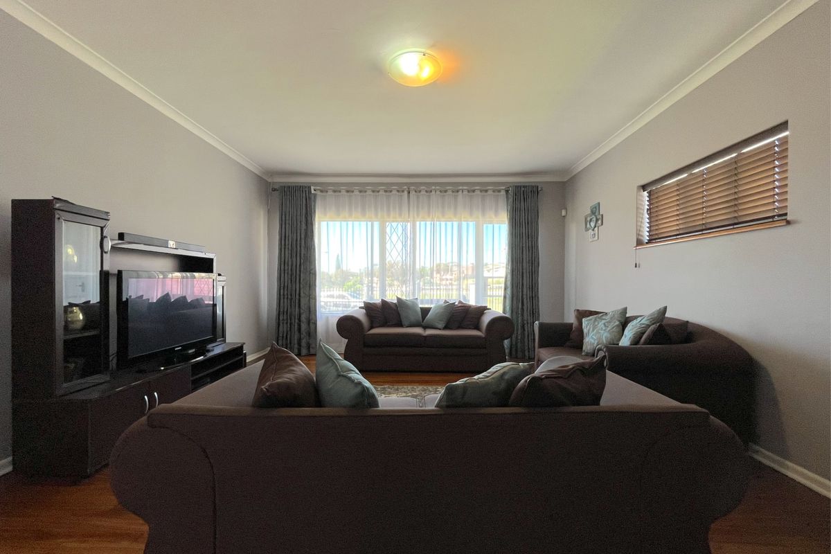 A spacious living room featuring hardwood flooring, large windows with fitted blinds, and neutral wall finishes.