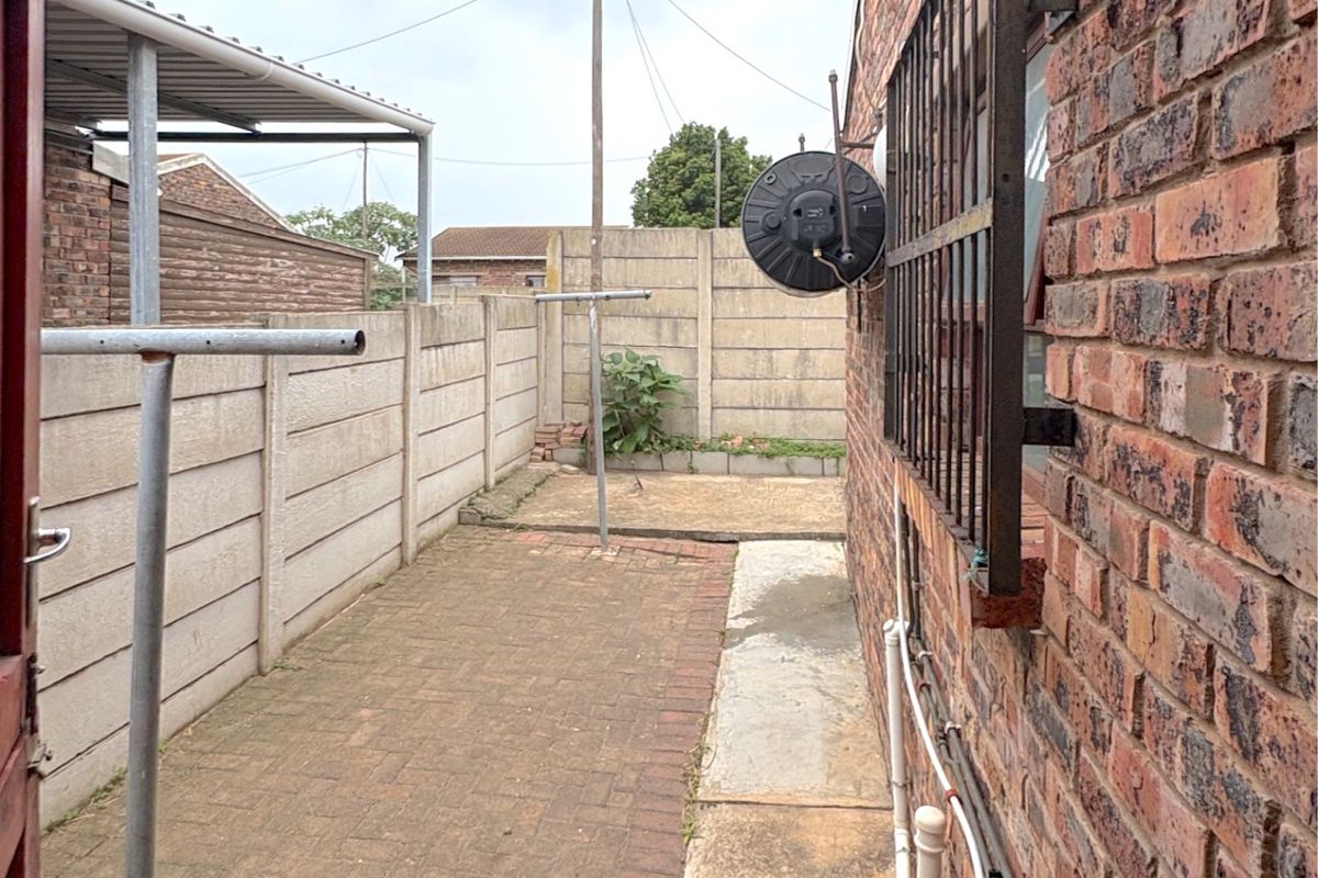 A narrow side exterior area featuring brick paving, precast concrete boundary walls, security bars on windows, and external plumbing fixtures.