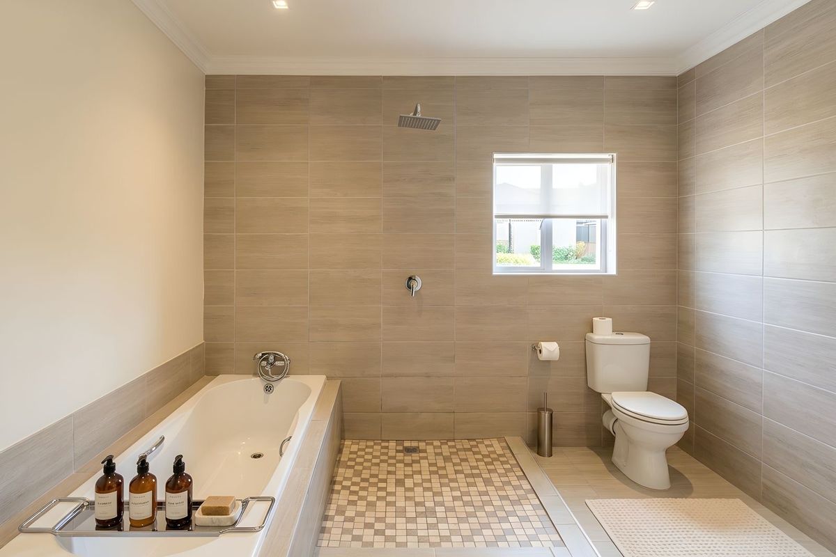 Modern bathroom featuring a built-in bathtub, a walk-in shower with mosaic tile flooring, and a standard toilet, finished with neutral wall tiles.