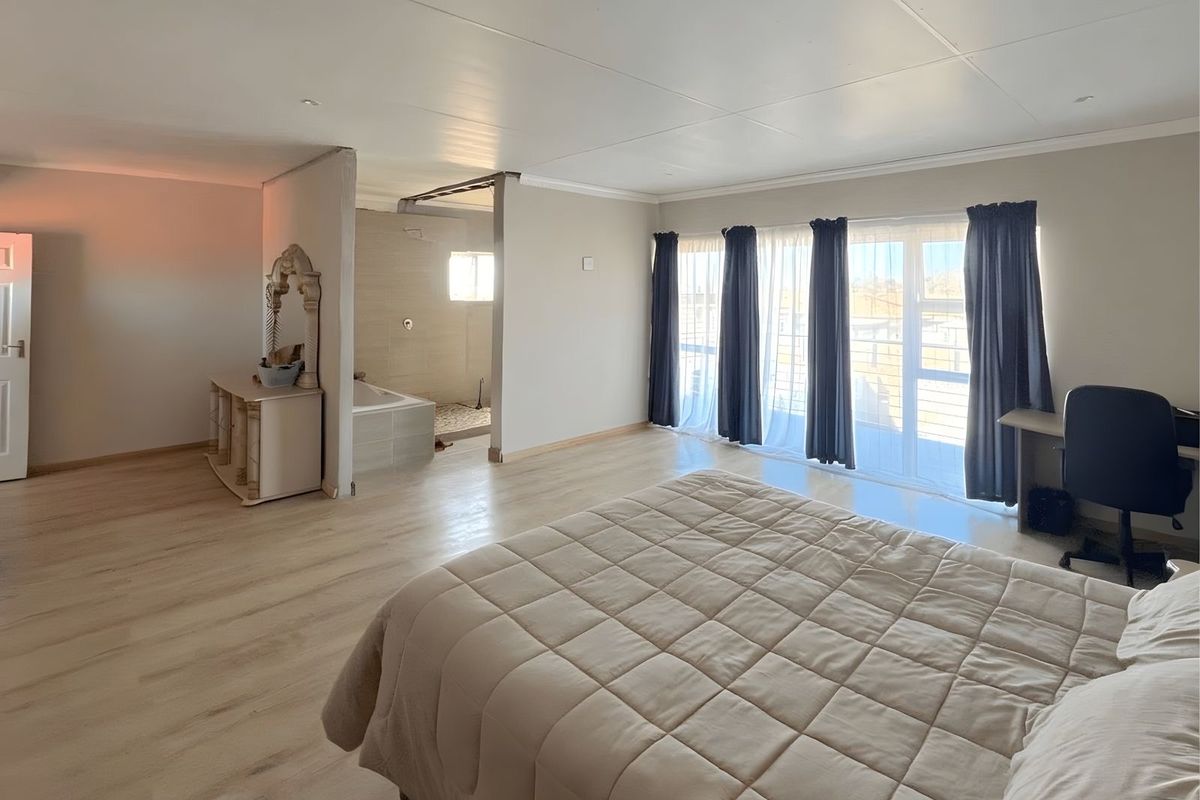 Spacious bedroom featuring an open-plan en-suite bathroom area, light wood-look flooring, and large windows with access to a balcony.