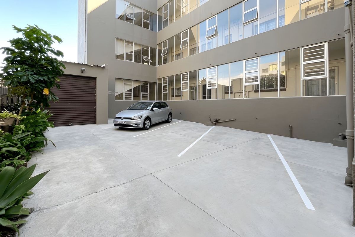 A paved exterior parking area at the rear of the apartment building, featuring marked parking bays and access to a garage.