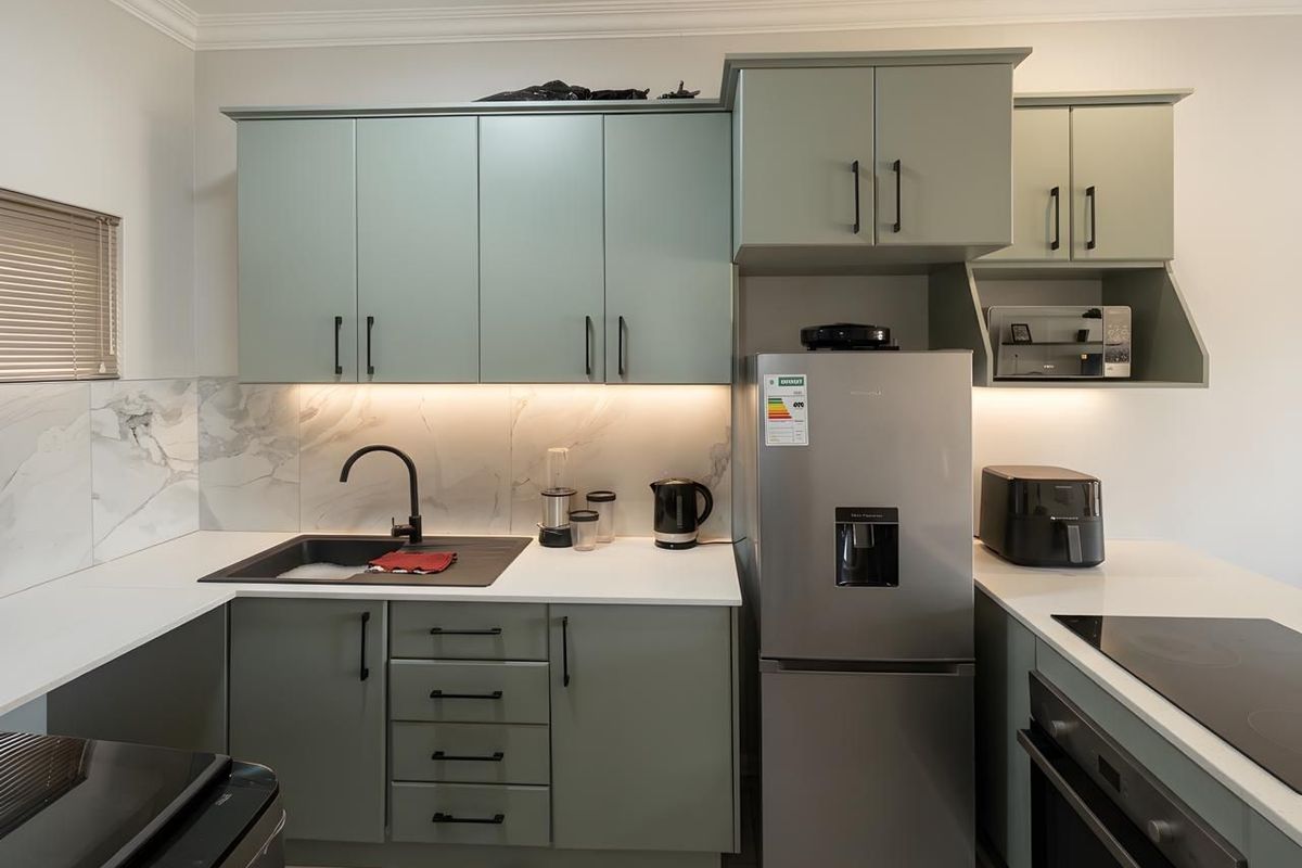 Modern kitchen featuring sage green cabinetry, marble-look splashback, integrated lighting, and high-quality matte black fixtures.