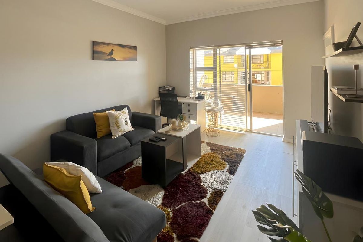 A bright living room featuring light-toned laminate flooring, crown molding, and a sliding glass door providing access to an outdoor balcony.